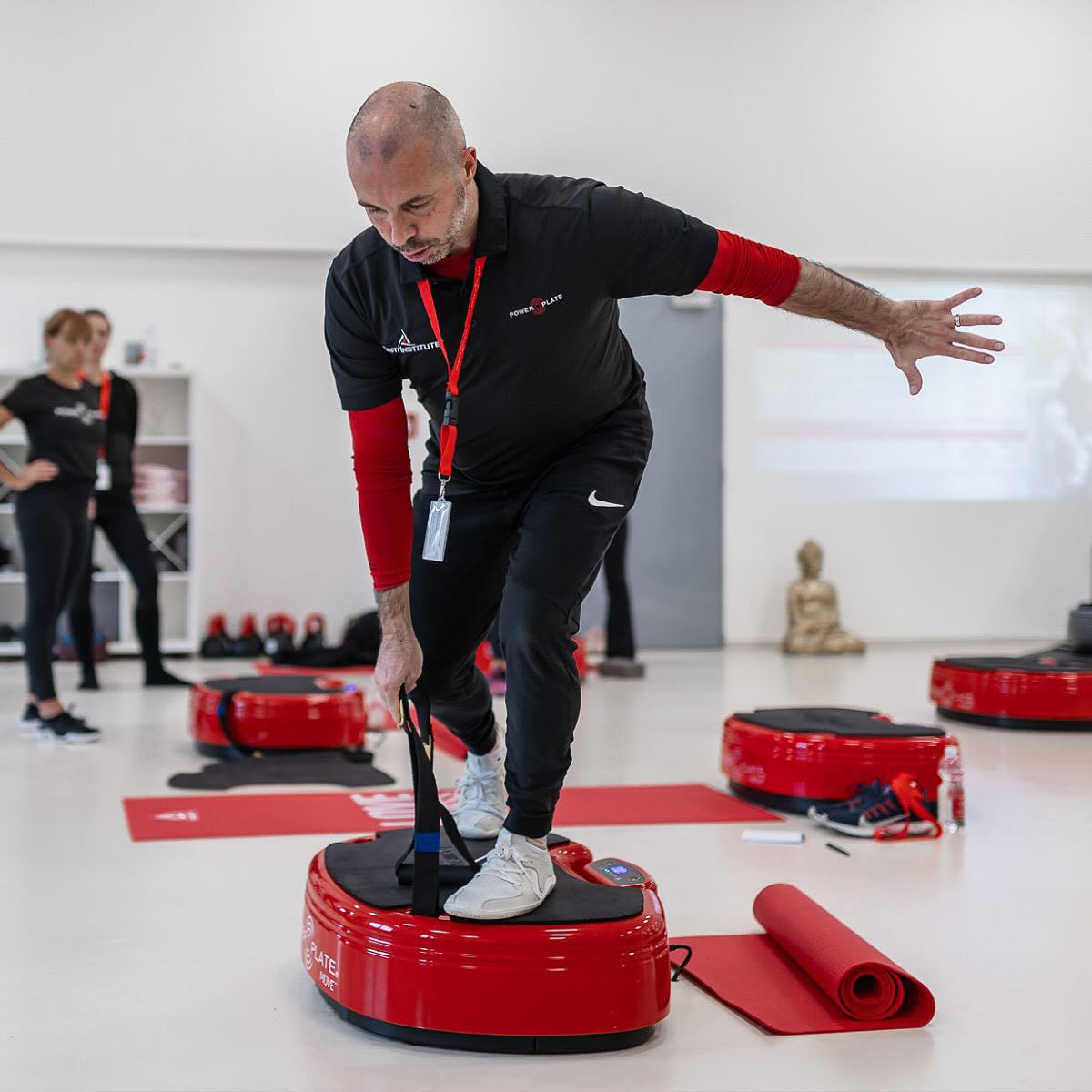 Man using a Power Plate Move from Athleticum fitness in a gym studio setting with other equipment and people in the background as part of whole body vibration training for bone and menopause and functional health.